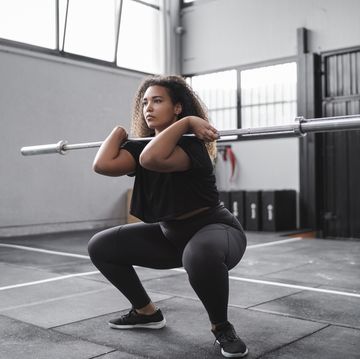 curly haired young woman practicing squats in gym