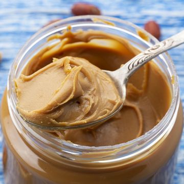 is peanut butter keto peanut butter in an open jar and peanuts in the skin are scattered on the blue table space for text